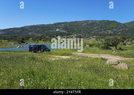 Camper parcheggiato su un prato verde vicino a un lago, circondato da montagne e alberi in una giornata di sole, il bacino idrico di Embalse de Plasencia, Embalse de Jerte, Rai¿½ Foto Stock