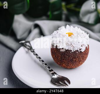 Squisito dessert al cocco su un piatto bianco guarnito con scaglie di cocco, abbinato a un tè Foto Stock