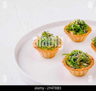 Antipasto elegante, insalata di alghe in conchiglie crostate, servita su un piatto bianco moderno Foto Stock