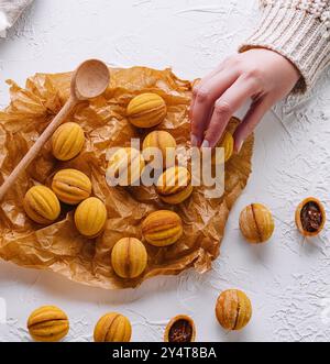 Colpo d'occhio di una mano che raggiunge i biscotti appena sfornati a forma di noce con caramello Foto Stock