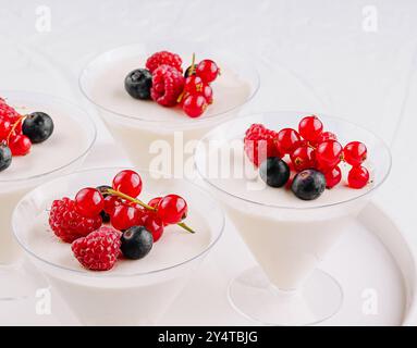 Eleganti tazze bianche da dessert ripiene di panna e ricoperte di ribes rosso, mirtilli e lamponi Foto Stock