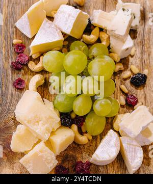 Selezione di formaggi e uve pregiati disposti su un tagliere rustico dall'alto Foto Stock