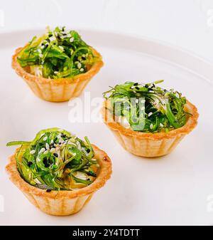 Antipasto elegante, insalata di alghe in conchiglie crostate, servita su un piatto bianco moderno Foto Stock