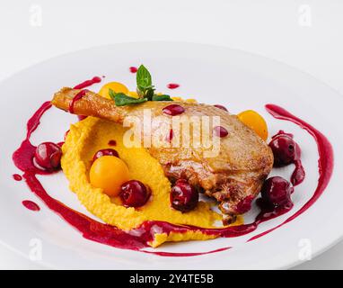 Elegante presentazione di anatra confit su un letto di purea cremosa con vivace salsa di frutti di bosco Foto Stock