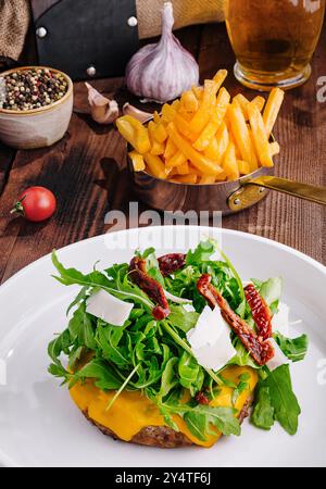 Delizioso cheeseburger con rucola e pomodori secchi su un tavolo rustico con contorni Foto Stock