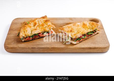 Panini deliziosi con pomodori, formaggio e verdure, tagliati e serviti su un tagliere di legno Foto Stock