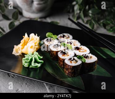 Disposizione artistica del sushi su un piatto nero con accenti verdi, perfetta per un menu sofisticato Foto Stock