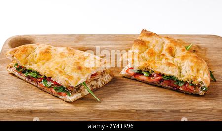 Panini deliziosi con pomodori, formaggio e verdure, tagliati e serviti su un tagliere di legno Foto Stock