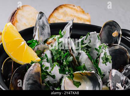 Immagine ravvicinata di succulente cozze al vapore guarnite con prezzemolo e servite con un cuneo di limone Foto Stock