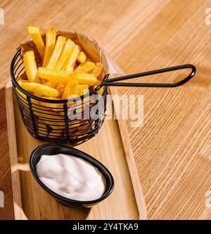 Patatine fritte croccanti servite in un elegante cestino con una crema su un tavolo di legno Foto Stock