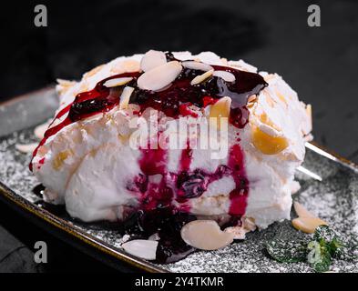 Elegante dessert pavlova con composta di bacche, mandorle affettate e zucchero a velo su un piatto scuro Foto Stock