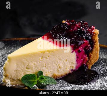 Fetta di cheesecake cremosa condita con una vivace composta di bacche e zucchero a velo, servita elegantemente su un piatto scuro Foto Stock