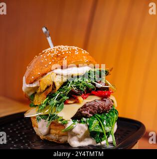 Hamburger artigianale su piatto nero con formaggio, verdure e pomodori secchi, in un ambiente accogliente Foto Stock