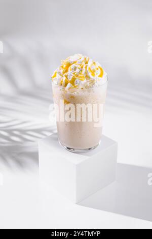 Bicchiere alto di milkshake al caramello con panna montata e salsa al caramello su sfondo bianco con ombre di foglie di palma Foto Stock