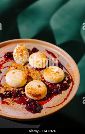 Pancake rotondi di formaggio cottage stesi su un piatto con marmellata di ciliegie, decorati con panna acida e briciole Foto Stock