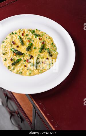 Risotto cremoso con asparagi e pancetta, servito su un piatto bianco su un tavolo di legno Foto Stock