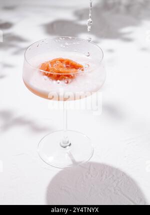 Lo champagne viene versato su una paletta di sorbetto rosso in un bicchiere coupé per preparare un cocktail rinfrescante Foto Stock