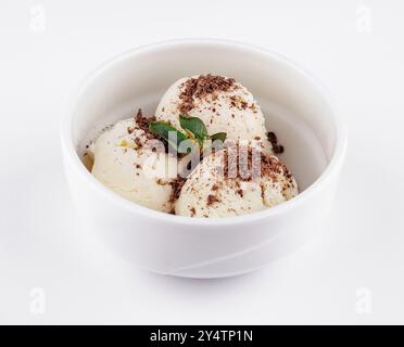 Tre cucchiai di gelato alla vaniglia ricoperti di scaglie di cioccolato e un rametto di menta serviti in una ciotola bianca Foto Stock