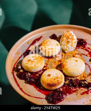 Pancake rotondi di formaggio cottage stesi su un piatto con marmellata di ciliegie, decorati con panna acida e briciole Foto Stock