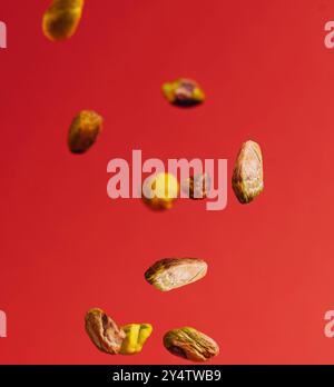 Pistacchi con conchiglie aperte che cadono su sfondo rosso Foto Stock