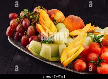 Fette di anguria, cantaloupe e pesche disposte con uva su un piatto, creando un colorato e rinfrescante dessert estivo Foto Stock