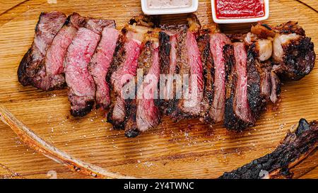 Bistecca di tomahawk grigliata a fette appoggiata su un tagliere di legno con due salse Foto Stock