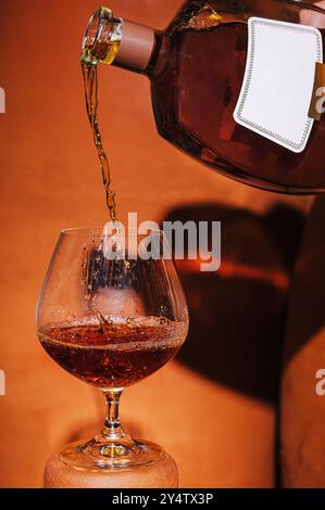 Il barista sta sta versando il brandy da una bottiglia con un'etichetta vuota in un bicchiere Foto Stock