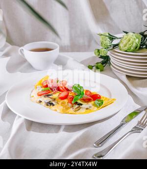 Omelette ripiena di ingredienti deliziosi, servita su un piatto bianco per colazione Foto Stock