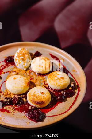 Pancake rotondi di formaggio cottage stesi su un piatto con marmellata di ciliegie, decorati con panna acida e briciole Foto Stock