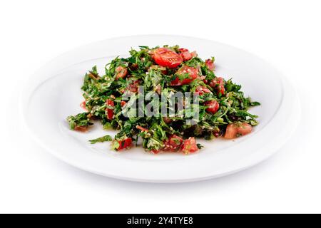 Insalata di tabbouleh appena preparata, composta da prezzemolo, pomodori e altri ingredienti freschi, ricoperta su un piatto bianco Foto Stock