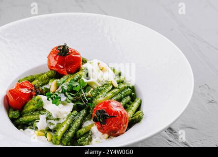 Delizioso pasto vegetariano con trofie e pesto al basilico, decorato con pinoli, pomodori ciliegini al forno e burrata, servito su bianco Foto Stock