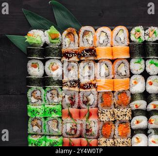 Grande set di sushi roll su un tavolo di legno nero decorato con foglie di bambù Foto Stock