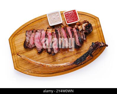 Bistecca di tomahawk grigliata a fette distesa su una tavola di legno con due salse Foto Stock