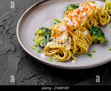 Gli spaghetti con salsa al pesto, i gamberetti e i broccoli decorati con scaglie di mandorle sono adagiati su un piatto grigio Foto Stock