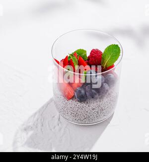 Budino di semi di Chia con lamponi freschi, mirtilli, fragole e foglie di menta in un bicchiere su sfondo bianco Foto Stock