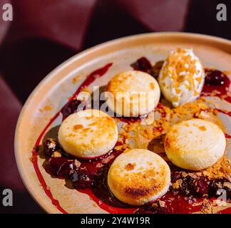 Pancake rotondi di formaggio cottage stesi su un piatto con marmellata di ciliegie, decorati con panna acida e briciole Foto Stock