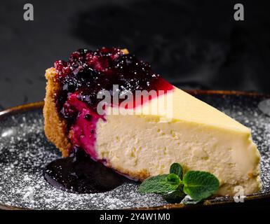Fetta di cheesecake cremosa condita con una vivace composta di bacche e zucchero a velo, servita elegantemente su un piatto scuro Foto Stock