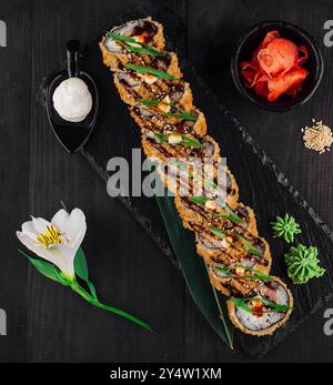 Pezzi freschi di sushi tempura maki con pesce e semi di sesamo decorati con fiori adagiati su un piatto di pietra nera Foto Stock