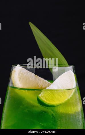 Il cocktail verde viene versato in un bicchiere con fette di ghiaccio, limone e lime su sfondo nero Foto Stock