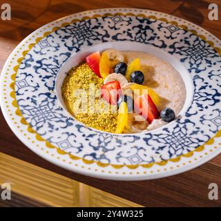 Porridge di farina d'avena ricoperto da bacche fresche, fette di banana, fette di arancia e pistacchi tritati in una ciotola, perfetto per una colazione sana e deliziosa Foto Stock