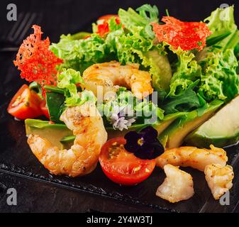 Insalata fresca con gamberetti, pomodori, avocado ed erbe aromatiche servita su un piatto di pietra nera Foto Stock