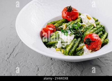 Delizioso pasto vegetariano con trofie e pesto al basilico, decorato con pinoli, pomodori ciliegini al forno e burrata, servito su bianco Foto Stock