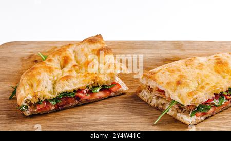 Panini deliziosi con pomodori, formaggio e verdure, tagliati e serviti su un tagliere di legno Foto Stock