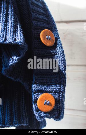 Pullover in maglia blu con bottoni in legno, primo piano. Cardigan in filato di lana con bottoni marroni alla luce del sole. Abbigliamento caldo e accogliente. Design in maglia fatto a mano Foto Stock