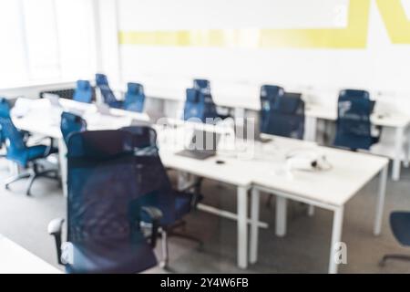 Spazio per ufficio, spazio di coworking o aula sfocati senza persone. Scrivanie per computer portatili e sedie da ufficio blu. Foto di alta qualità Foto Stock