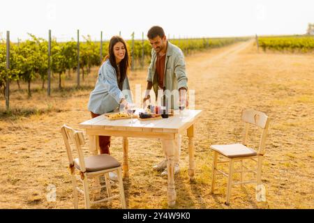 Crogiolandosi nella calda luce del sole, una coppia gioiosa si abbraccia mentre si divertono in un delizioso picnic tra le viti, assaporando vino e prelibatezze gourmet Foto Stock