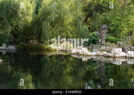 Un laghetto in un parco cinese con un giardino roccioso e salici piangenti riflessi nell'acqua. Splendido paesaggio estivo, luogo in cui rilassarsi. Foto di alta qualità Foto Stock