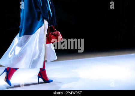 Outfit elegante, gonna lunga bianca, tacchi alti e borsa rossa, modello alla moda che cammina sulla passerella Foto Stock