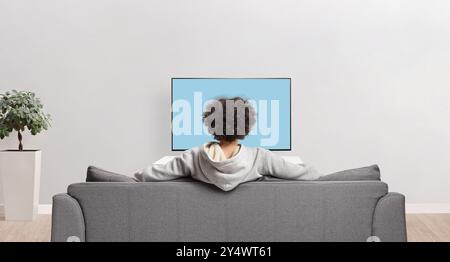 Ripresa con vista posteriore di un ragazzo che guarda la televisione e si siede su un divano in un appartamento Foto Stock