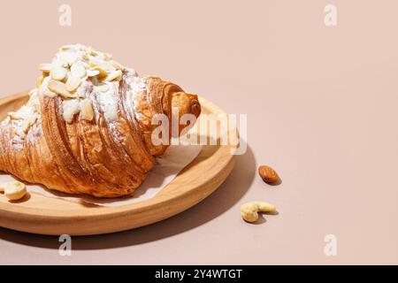 Piatto di legno di croissant dolce con zucchero a velo e diverse noci su fondo rosa Foto Stock